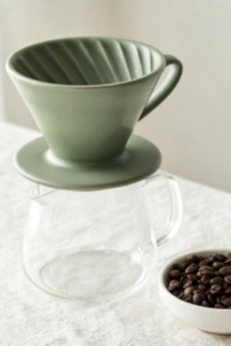 Slightly soft product photo of a sage-green ceramic pour-over dripper — before